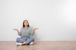 © New Africa - Young woman sitting on floor near white wall indoors. Space for text