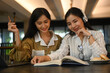 © Prathankarnpap - Two happy woman students reading book, preparing for exams in the university library. Education and people concept