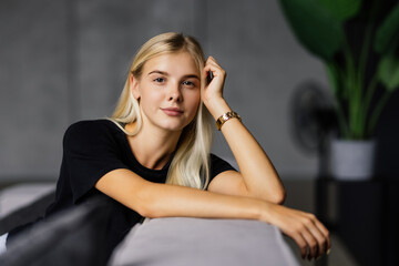 Smiling blonde young woman wearing casual clothes relaxing on a couch at home