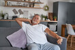 © gpointstudio - Senior man stretching at morning and sitting at couch