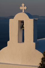 Wall Mural - A cross and a bell on the top of an orthodox church in Ios Greece while the sun is setting in the background