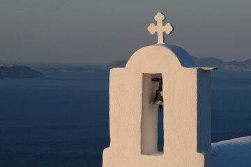 Wall Mural - A cross and a bell on the top of an orthodox church in Ios Greece while the sun is setting in the background