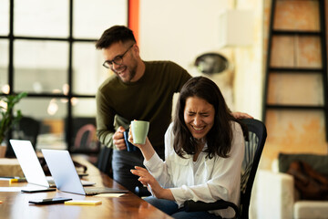 Wall Mural - Colleagues laughing in office. Businesswoman and businessman drinking coffee