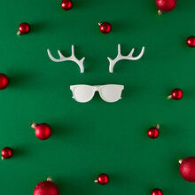 Creative Reindeer Christmas Concept Made With Hipster Glasses, Antler And Christmas Balls On Green Background. Minimal Flat Lay. New Year Holiday Idea. Greeting Card.