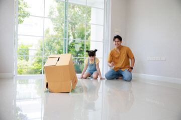 Wall Mural - Happy asian father playing with cute small kids daughters and son laughing on moving day, boy having fun hide and seek  in box in new house.