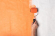 Painting wall with roller. Hand with roller painted wall in orange color. Renovation home.