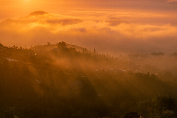 Wall Mural - Golden sunrise over white puffy clouds with distant mountains on horizon. Sun ray through the mist in the mountains