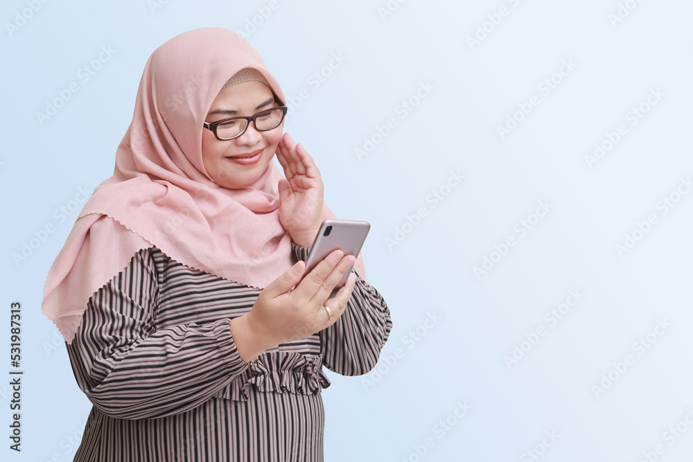 Portrait of cheerful Asian woman with hijab, holding mobile phone and ...