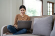 © Natee Meepian - Happy asian woman using laptop in the sofa with a happy face standing and smiling with a confident smile showing teeth