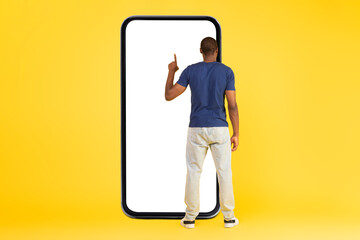 African Man Using Large Smartphone Over Yellow Background, Back View