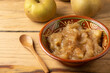 Close-up of rustic bowl with cinnamon applesauce on table with pippin apples and wooden spoon, horizontal
