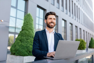 Wall Mural - Cheerful confident handsome young caucasian guy with beard in suit typing on laptop