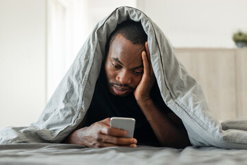 Aufkleber - Black Guy Using Smartphone Lying Covered With Blanket In Bedroom