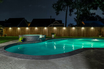 A backyard swimming pool and jacuzzi hot tob at night