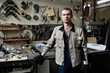 © Seventyfour - Waist up portrait of young male worker standing in workshop and looking at camera, tools in background, copy space