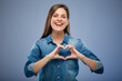 Smiling woman in blue denim shirt making heart shape with her hands. Isolated portrait.