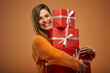 Happy woman holding stack of gift boxes. Isolated female portrait in christmas style on orange background.