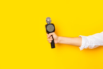 Man's hand holds a microphone in a hole in a torn bright yellow cardboard background
