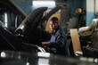 © Seventyfour - Side view portrait of young female mechanic repairing truck engine in garage with accent light and looking under hood