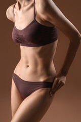 Wall Mural - Slim young woman in underwear on brown background