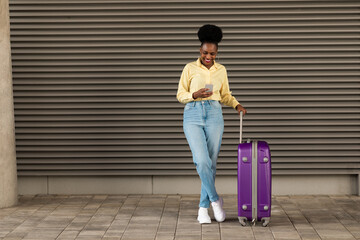 Wall Mural - African American Female Tourist Using Cellphone Standing With Suitcase Outdoors