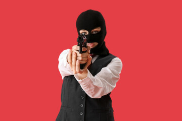Wall Mural - Young woman in balaclava aiming gun against red background