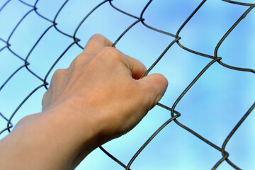 Close-up woman's hand holding on to the bars of a metal mesh.