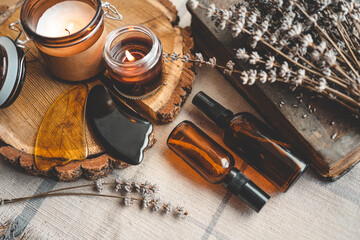 Set of natural face care products, gua sha scraper, oil jars, lavender and a candle on a wooden background