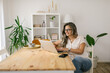 © STUDIO TAURUS - Happy woman texting on social media via laptop at home