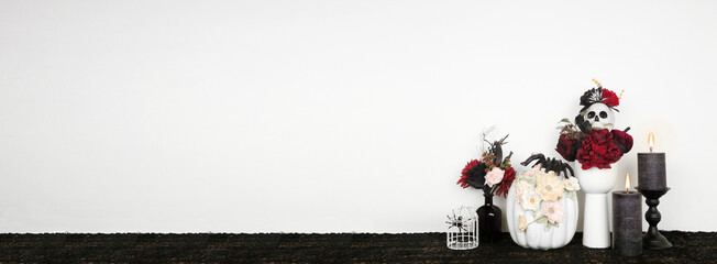 Halloween gothic romance shelf decor with copy space against a white wall banner background. Black shelf with red and black flowers, spiders, floral pumpkin and candles.