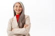 Portrait of successful asian senior businesswoman, smiling and looking happy, professional power pose, corporate outfit, standing over white background