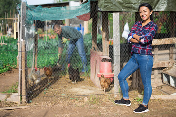 Wall Mural - Latina woman farmer in checked shirt feeding chickens at farm