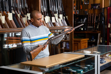 Wall Mural - Portrait of focused male standing with rare collectible rifle in hunting shop indoors