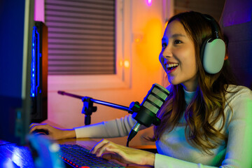 Asian young gamer woman wear headphones playing video games online on computer she live stream and chat with fans, Happy streamer female talking with microphone in gaming room, game streaming concept