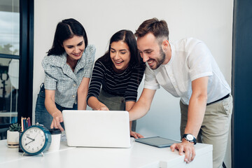 Wall Mural - Happy diverse friends watching funny video, laughing at joke, using laptop and having fun together, brainstorm together at meeting	