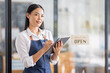 © David - Asian woman is a waitress in an apron, the owner of the cafe stands at the door with a sign Open waiting for customers. Small business  cafes and restaurants concept,