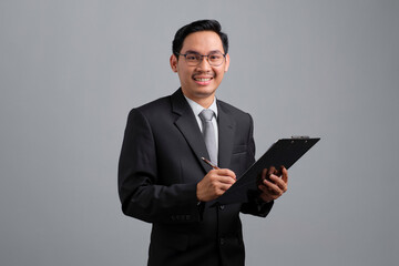 Portrait of smiling handsome young businessman in formal suit with clipboard isolated on grey background