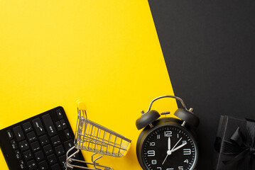 Wall Mural - Black friday concept. Top view photo of keyboard shopping cart alarm clock and giftbox with ribbon bow on bicolor yellow and black background with copyspace