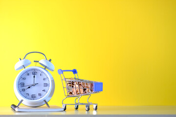 Canvas Print - Cart with coin and alarm clock on yellow background