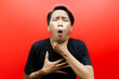 Ew. It's so gross. A young Asian man in a t-shirt stands over an empty red background while displaying an expression of dislike and disgust. man is showing vomit gesture.