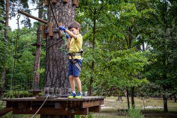 Wall Mural - Strong excited young boy playing outdoors in rope park. Caucasian child dressed in casual clothes and sneakers at warm sunny day. Active leisure time with children concept