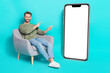 Photo of nice promoter man sit armchair indicate fingers placard empty space wear pullover isolated blue color background