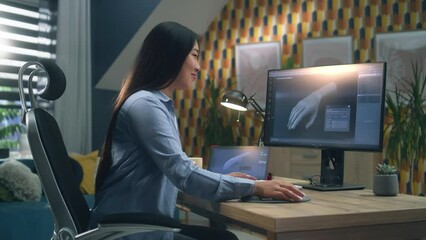 Poster - Asian woman sitting on chair at the table at home office and making 3D prototype of human hand in professional program for 3D modelling, using modern computer and digital tablet.
