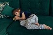Portrait of upset, sad and depressed barefoot little boy lying on green sofa, sucking thumb finger. Psychological stress