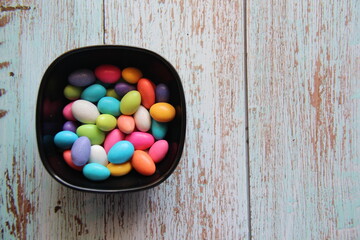 Colorful sugared almonds in a black bowl on a wooden table top view and copy space.