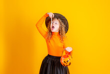 Teenage Girl In A Witch Costume On A Yellow Background, Holding A Confent Pumpkin Eating Marmalade Worms Halloween Party