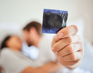 Wall Mural - Condom, safety and safe sex with couple in bed, foreplay and intimate bonding in their home together. Passionate man showing protection in hand while kissing and being sexual with a woman in bedroom