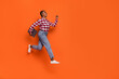 © deagreez - Full body profile photo of energetic pretty girl hurry jumping look empty space isolated on orange color background