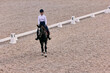Aerial view. Female rider on horseback riding trot around the sandy arena in countryside, in summer day, outdoors. Dressage of horses. Horseback riding