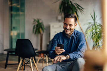 Smiling adult man holding his glasses and using a mobile phone.